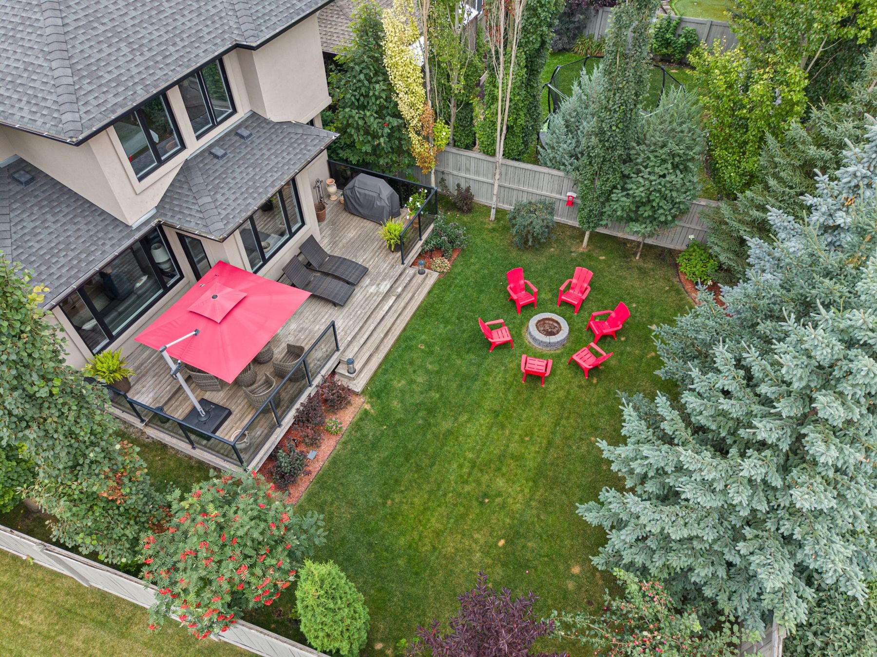 Aerial view of a landscaped Edmonton backyard with a deck and red chairs around a fire pit